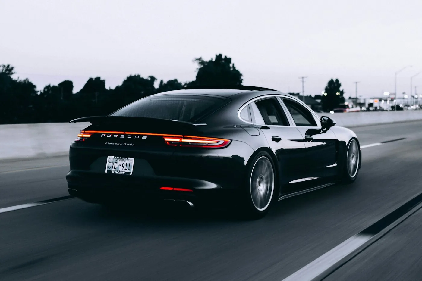 Rear three-quarter view of a dark Porsche 911 on a tree-lined road