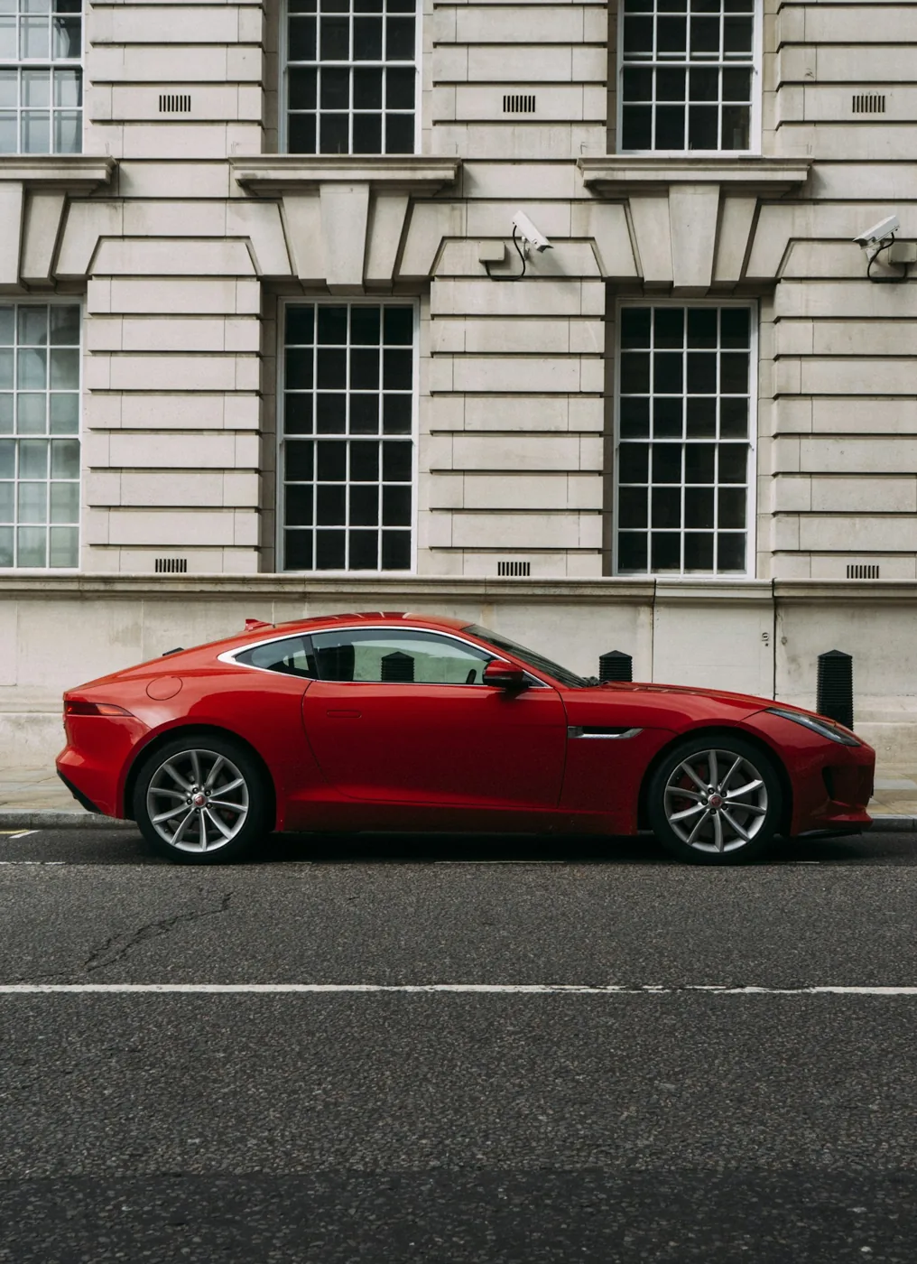 Side profile of a red Aston Martin beside a stone building